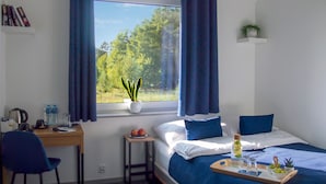 Une chambre à coucher avec un lit, un bureau, une chaise, une fenêtre avec des rideaux, une plante en pot et un plateau avec des fruits et une bouteille.