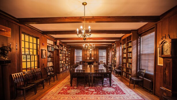 A library with wooden bookshelves, a large wooden table, and a chandelier. - Crow's Nest Newport (Newport)