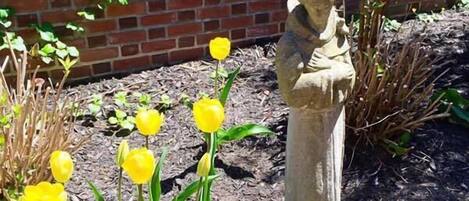 Um jardim com uma estátua, tulipas amarelas e um muro de tijolos.