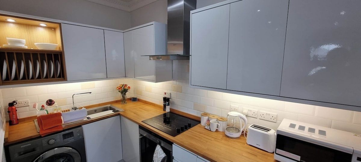 A modern kitchen with grey cabinets, a wooden countertop, a built-in oven, and a dishwasher.