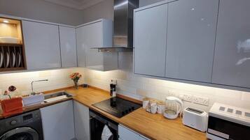 A modern kitchen with grey cabinets, a wooden countertop, a built-in oven, and a dishwasher.