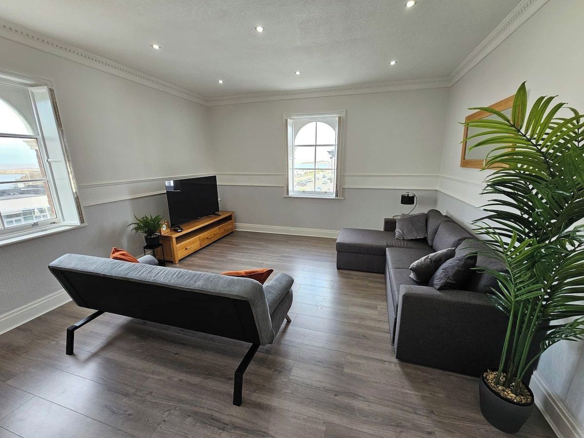 A modern living room with a sofa, a bench, a television, and a potted plant.