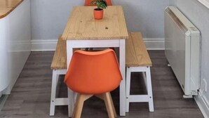 Un coin repas avec une table en bois et des chaises orange, un tableau au mur et un radiateur blanc.