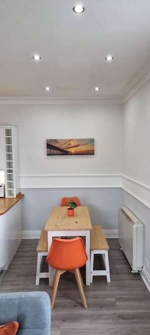 A dining area with a wooden table and orange chairs, a painting on the wall, and a white radiator. - Lakeview Court, Sea+Lake view, free parking (Southport)