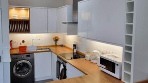A modern kitchen with white cabinetry, a wooden countertop, and a built-in washing machine. - Lakeview Court Southport (Southport)