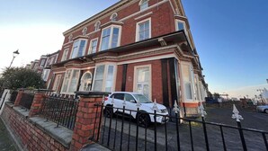 Un bâtiment en briques de deux étages, avec une voiture blanche garée devant.