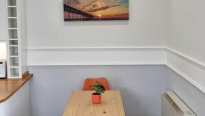 A dining area with a wooden table and orange chairs, a white radiator, and a painting on the wall. - Lakeview Court Southport (Southport)