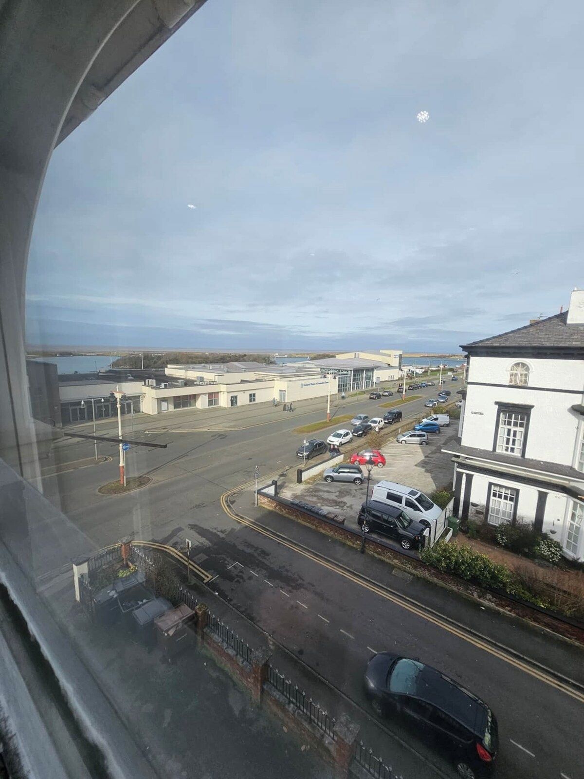A view of a parking lot with several cars, a building with a white facade, and a clear sky.