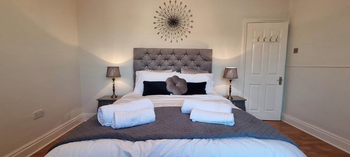 A bedroom with a tufted headboard, two bedside tables with lamps, a door, and a decorative wall piece.