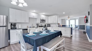 A modern kitchen with white cabinets, stainless steel appliances, and a dining area set with a blue tablecloth and white chairs. - Spacious 4BR/2BA home ideal for families, contractors & extended stays. King primary + 3 queen BRs with Smart TVs & mini fridges. Fast WiFi, full kitchen, washer/dryer, backyard & deck. (Clarksville)