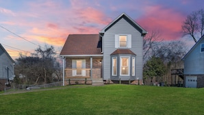 A two-story house with a front porch, a bay window, and a well-maintained lawn. - Spacious 4BR/2BA home ideal for families, contractors & extended stays. King primary + 3 queen BRs with Smart TVs & mini fridges. Fast WiFi, full kitchen, washer/dryer, backyard & deck. (Clarksville)