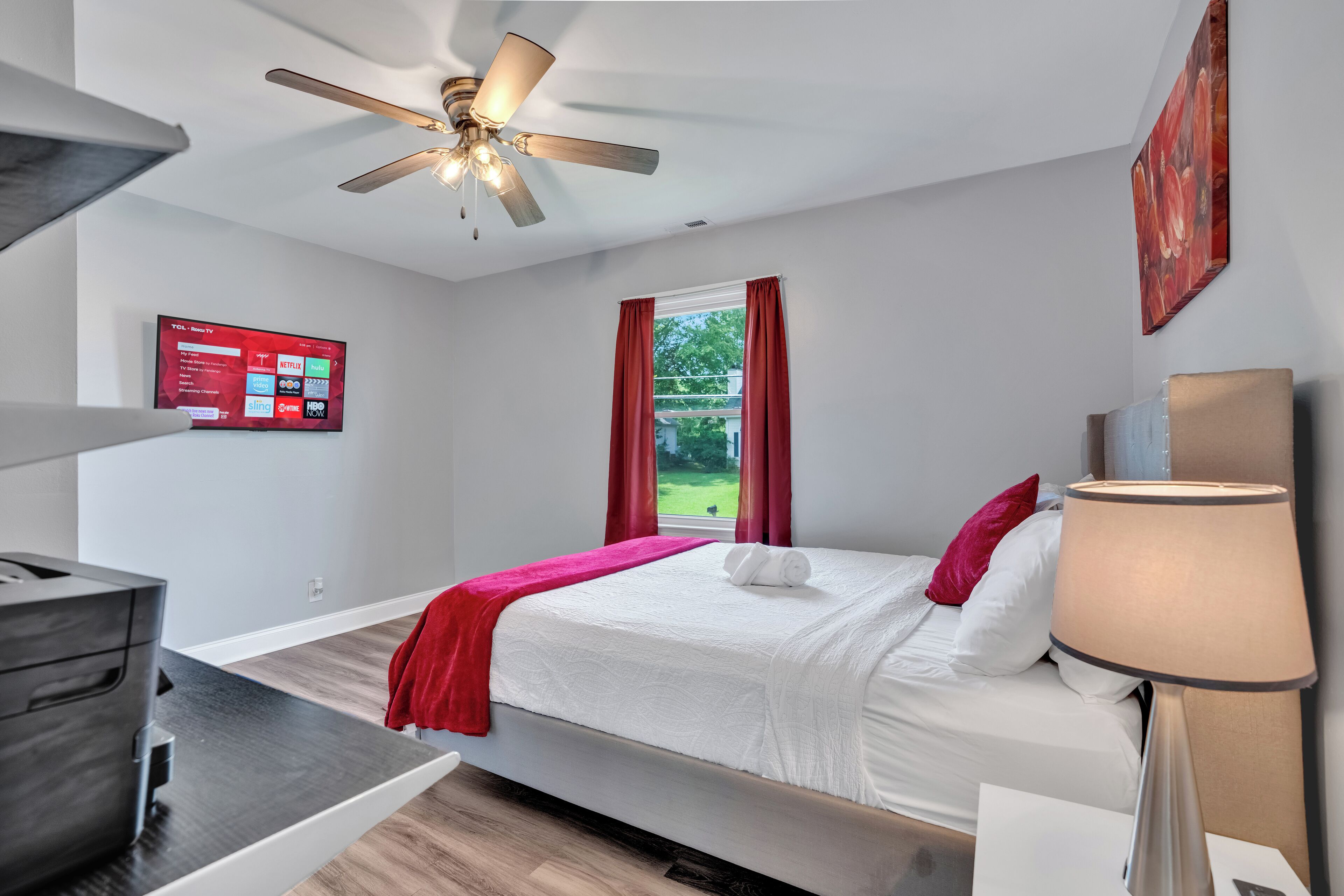 Une chambre d’hôtel équipée d’un lit, d’un bureau, d’un ventilateur de plafond, d’un téléviseur fixé au mur et d’une fenêtre avec des rideaux.