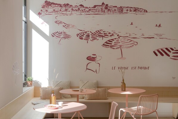 A cozy café with a mural of a beach scene, seating with cushions, and a view of the city. - Slo Hostel Nice (Nice)