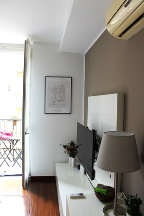 A modern living room with a flat-screen TV, a lamp, and a framed artwork on the wall.