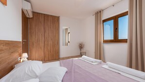 Una habitación de hotel con una cama, un armario de madera, un espejo, una ventana con cortinas y una mesita con lámpara.