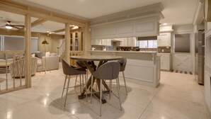 A spacious kitchen with a central island, white cabinetry, and a dining area with chairs.
