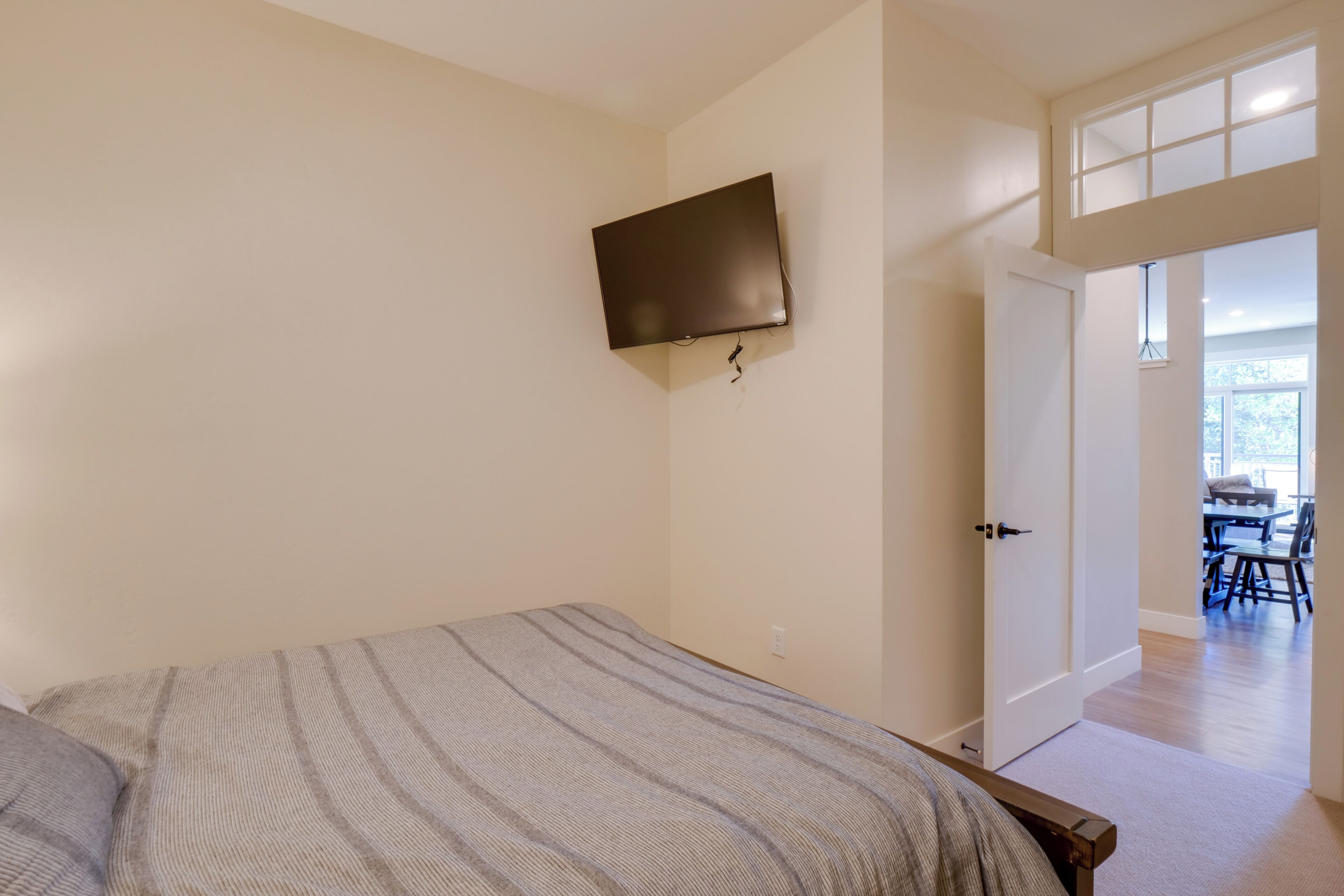Un dormitorio con cama, televisor montado y puerta que da a un comedor.