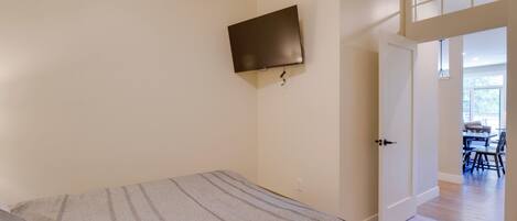 Un dormitorio con cama, televisor montado y puerta que da a un comedor.
