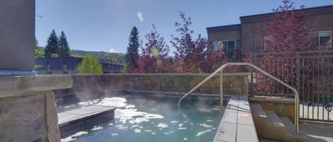 A hot spring area with a stone wall, steps leading into the water, and a metal railing.