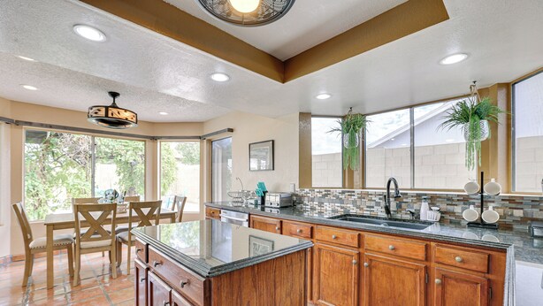 A spacious kitchen with wooden cabinets, a large island, and a tiled backsplash. - Family-friendly Home w/ Pool & Fire Pit in Peoria (Peoria)