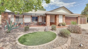 A two-story house with a brick facade, a covered patio with outdoor furniture, and a landscaped garden with a circular lawn area. - Family-friendly Home w/ Pool & Fire Pit in Peoria (Peoria)