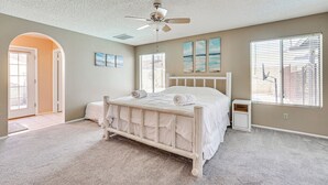 A bedroom with a wooden bed, a ceiling fan, a window with blinds, and a door leading to another room. - Family-friendly Home w/ Pool & Fire Pit in Peoria (Peoria)