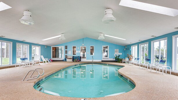 Une piscine intérieure aux murs d’un bleu clair, dotée de nombreuses fenêtres et d’un éclairage au plafond.