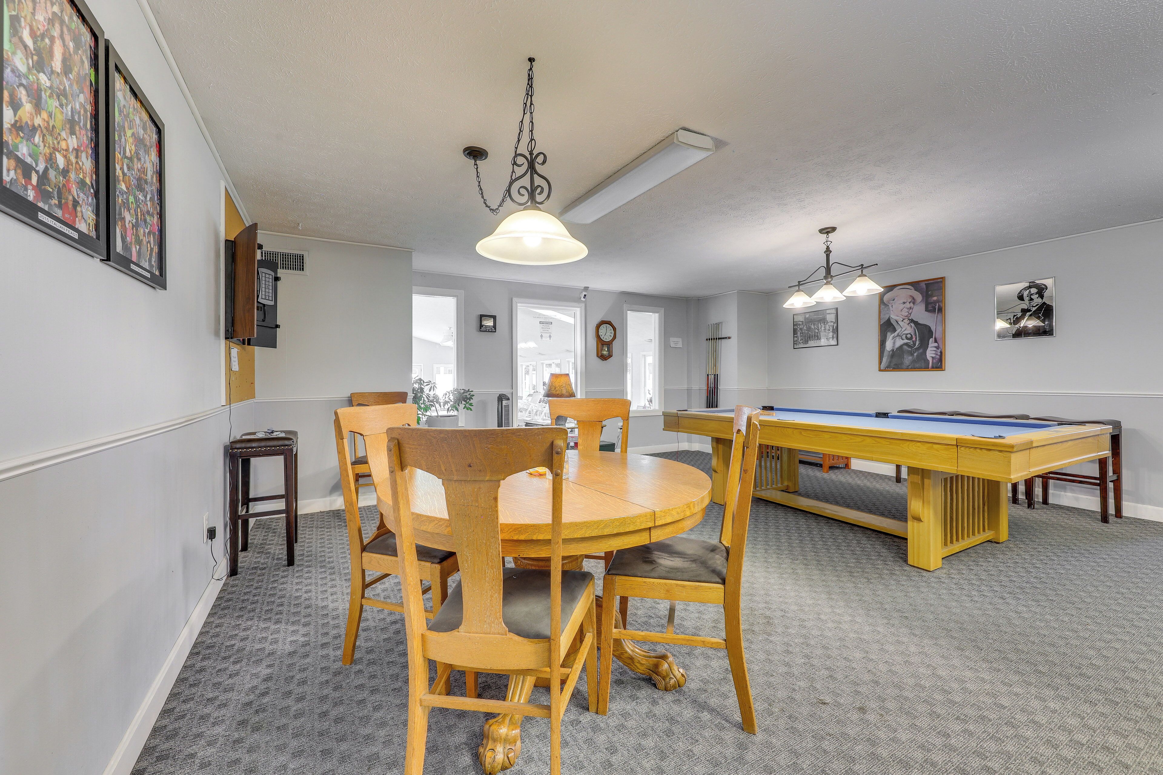A room with a pool table, wooden chairs, a round table, and framed pictures on the walls.