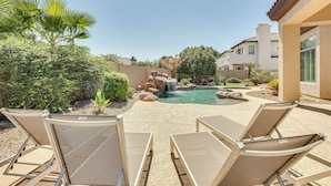 An outdoor pool area with lounge chairs, a waterfall, and surrounding greenery. - Private Pool & Patio at Home Near Goodyear (Litchfield Park)