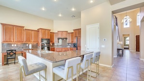 A spacious kitchen with granite countertops, wooden cabinets, and a central island with bar stools. - Private Pool & Patio at Home Near Goodyear (Litchfield Park)