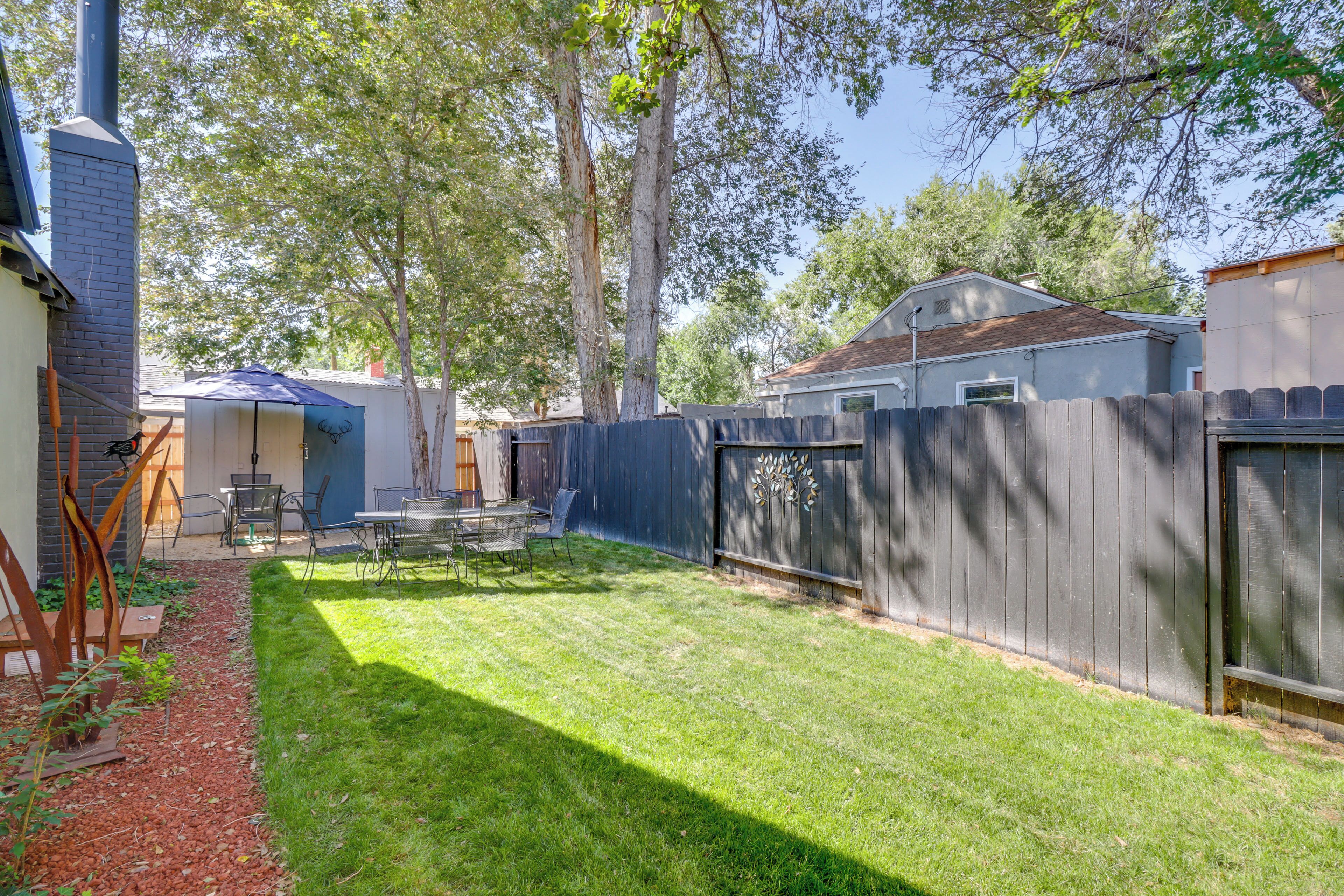 A backyard with a wooden fence, a grill, and a patio area with chairs and tables.