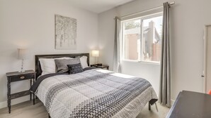 Une chambre à coucher comprenant un lit, des tables de chevet, une fenêtre avec des rideaux et une œuvre d’art accrochée au mur.