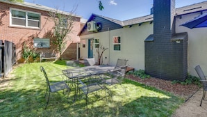 Un jardin avec une table et des chaises en métal, une maison en briques et un auvent bleu.