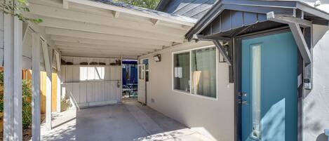 A covered patio area with a blue door, a small porch, and a window overlooking the backyard.