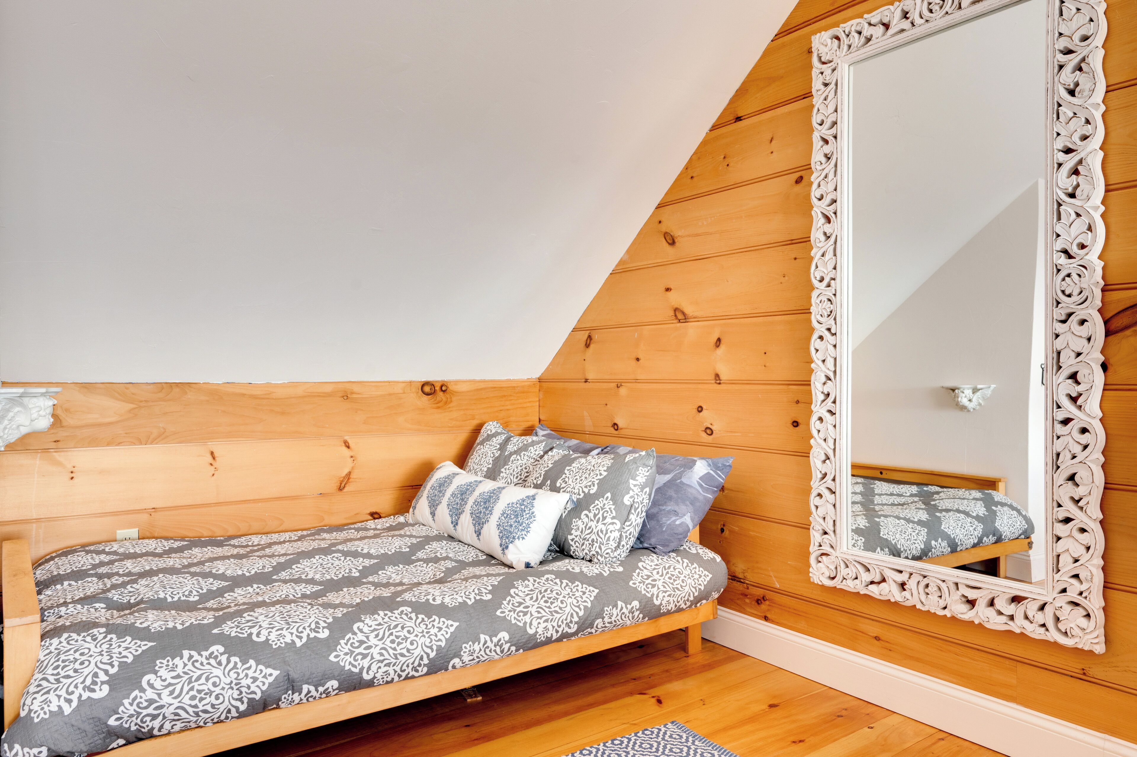 Een slaapkamer met een schuine kap, houten wanden, een bed met beddengoed met een patroon en een grote, versierde spiegel.