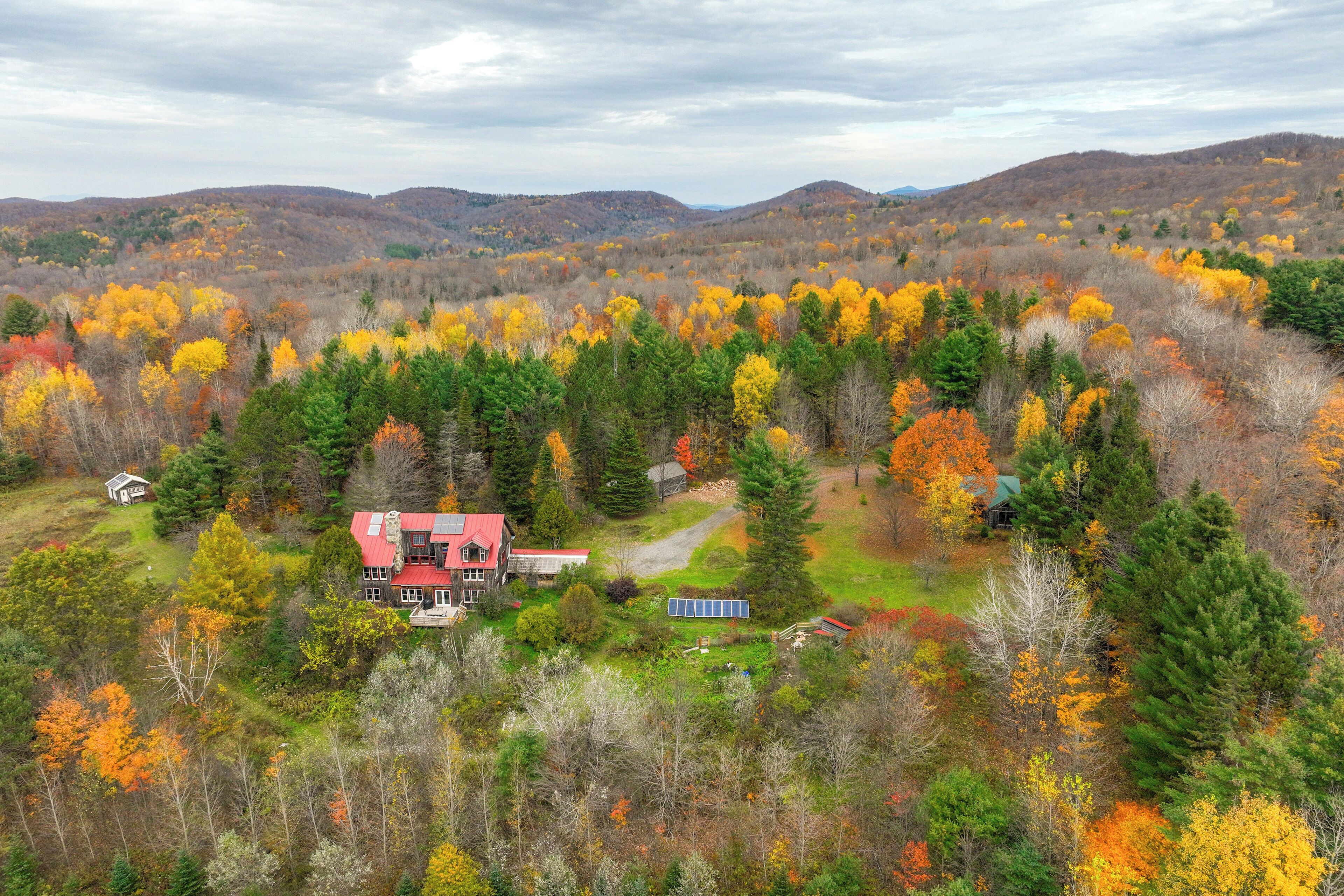 Une grande maison avec un toit rouge, entourée d’une forêt aux couleurs automnales.