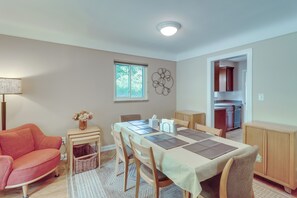 A dining area with a table set for four, a sofa, a lamp, and a window with a view of trees.