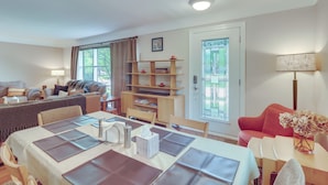 A well-lit living room with a dining area, a sofa, a red armchair, a bookshelf, and a door with a window. - Royal Oak Home: 13 Mi to Downtown Detroit (Royal Oak)