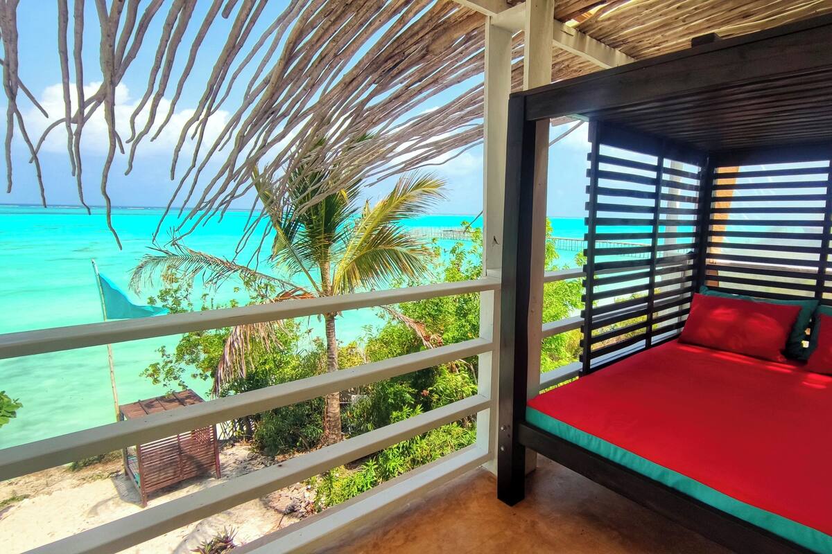 Una habitación con cama, vista al océano y balcón con barandilla.