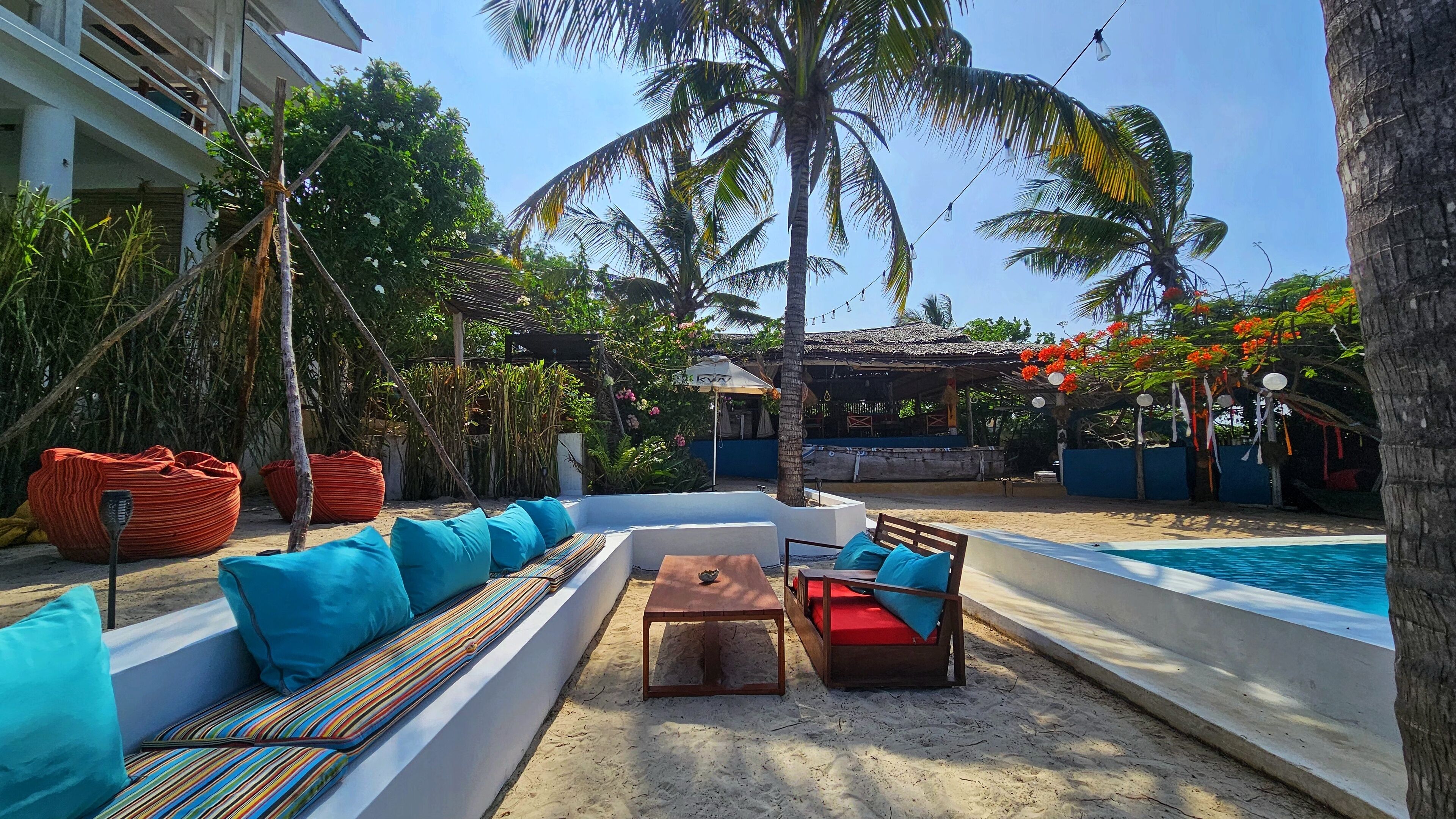 Un espace aménagé au bord de la piscine, avec un banc blanc, des coussins colorés et une table en bois.