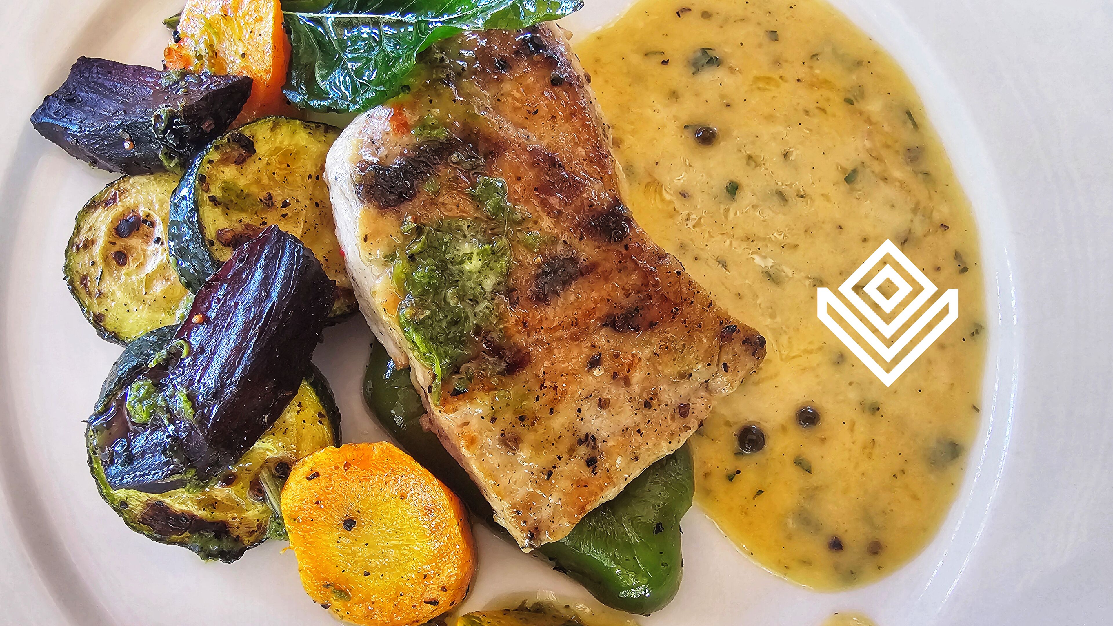 A plate with grilled fish, roasted vegetables, and a creamy sauce.