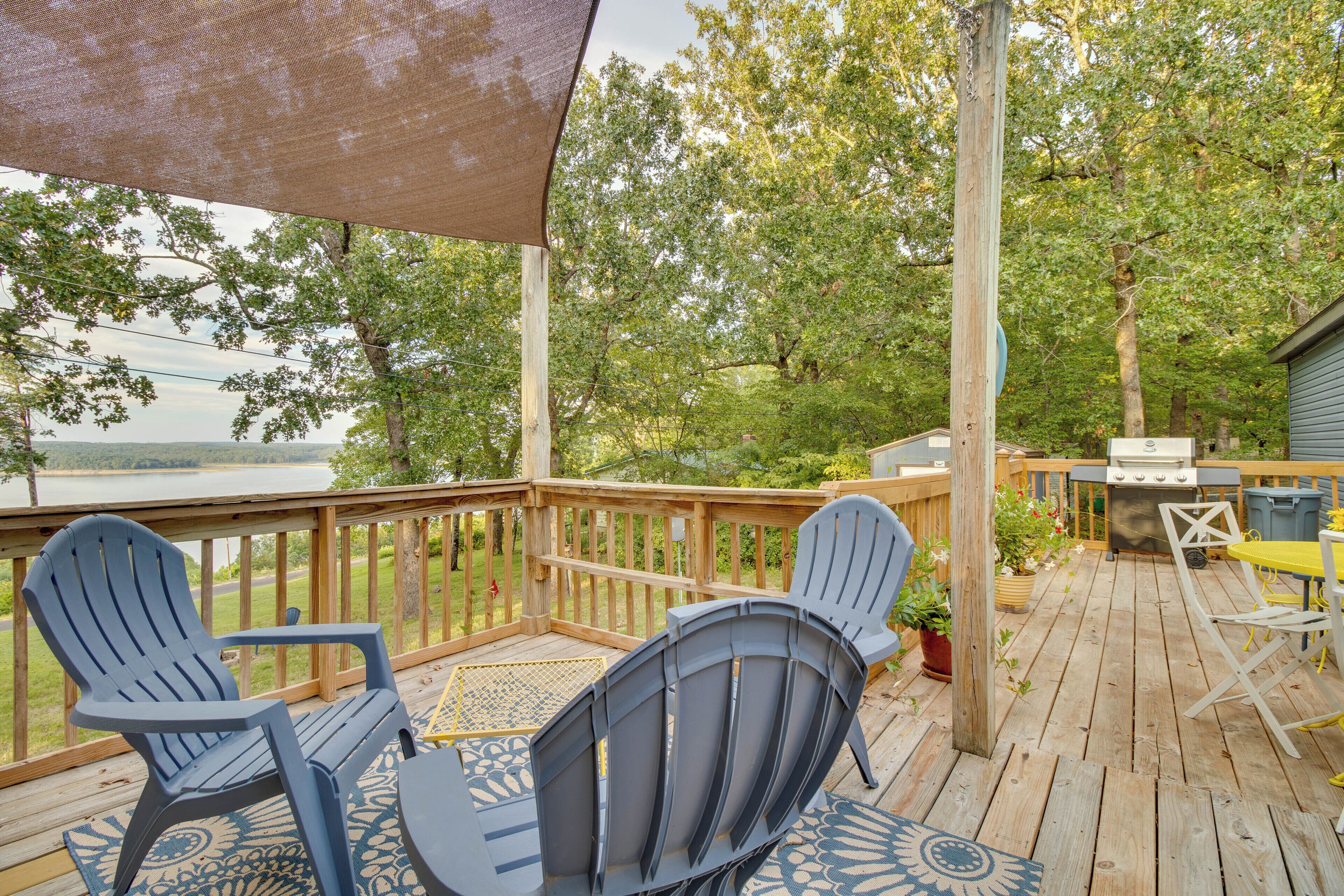 A wooden deck with Adirondack chairs, a grill, and a view of a lake.