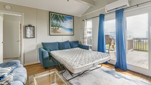 Et soveværelse med seng, sofa, et maleri af en strand, et ur og udsigt til det fri.