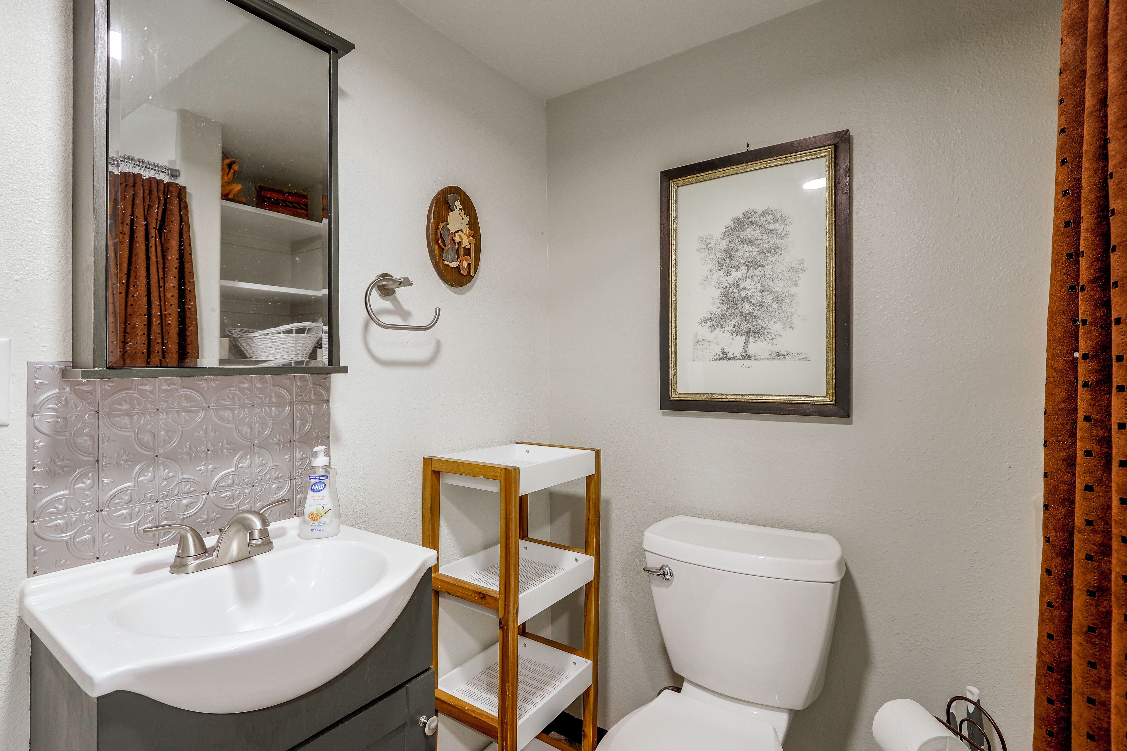 A bathroom with a white sink, a toilet, a mirror, and a framed botanical illustration on the wall.