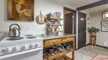 A kitchen with a stove, shelves with kitchenware, a framed painting, and a door with a sign.