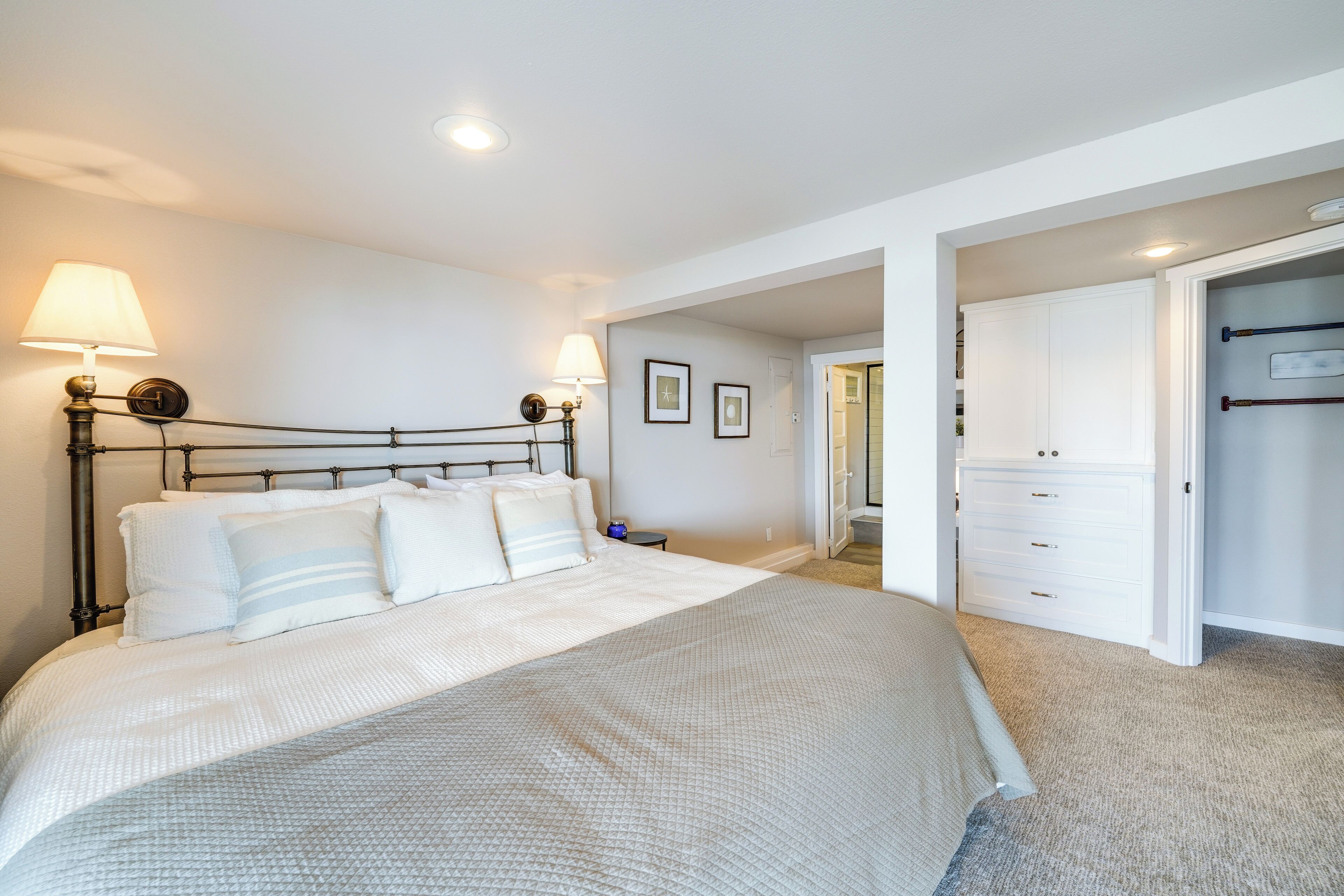 Un dormitorio con una cama grande, lámparas de noche, un armario y una puerta que da a otra habitación.