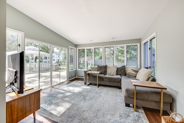 A spacious living room with a large window, a sofa, a coffee table, and a TV on a wooden stand.