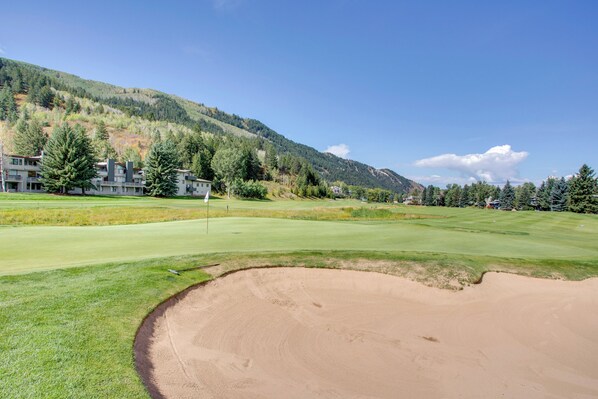 Un parcours de golf avec des bunkers, un mât de drapeau et une chaîne de montagnes en arrière-plan.