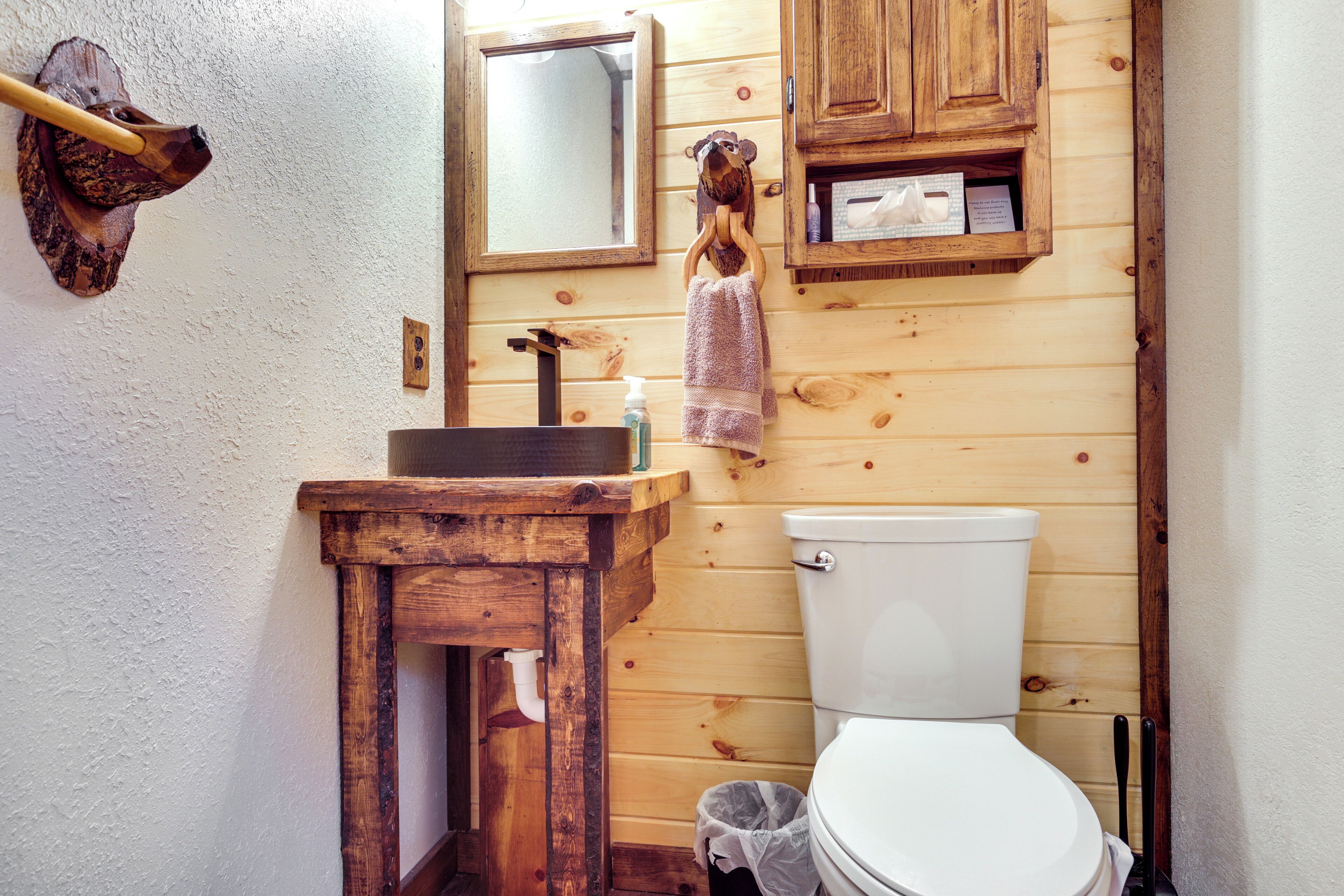 A wooden bathroom with a wooden sink, a mirror, and a toilet.