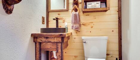 A wooden bathroom with a wooden sink, a mirror, and a toilet.